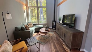 En hyggelig stue med en grøn sofa, et sofabord og et fjernsyn på et træskab.