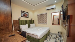 Una habitación de hotel con cama, escritorio de madera, televisor y basurero.