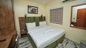 Una habitación de hotel con una cama, un escritorio de madera, un espejo y un equipo de aire acondicionado.