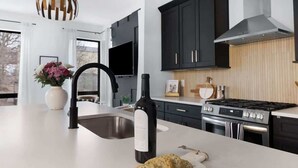 A modern kitchen with a large island, black cabinets, a stainless steel sink, and a gas stove. - The Chorus & The Duet - Mins from Downtown! (Nashville)