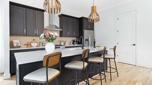 A modern kitchen with dark cabinets, a large island with bar stools, and pendant lighting. - The Chorus & The Duet - Mins from Downtown! (Nashville)