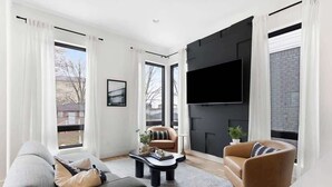 A modern living room with a sofa, armchair, and coffee table. There is a flat-screen TV mounted on the wall and a fireplace. - The Chorus & The Duet - Mins from Downtown! (Nashville)