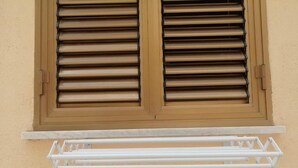 A window with horizontal blinds and a white towel rack below it. - Da Nina (Lascari)