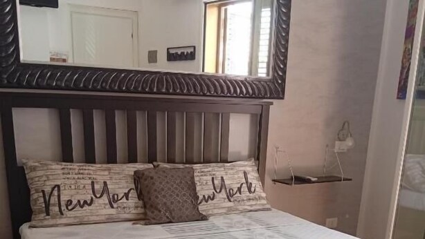 A neatly made bed with a grey quilt, two rolled towels, and pillows with 'New York' text. - Da Nina (Lascari)