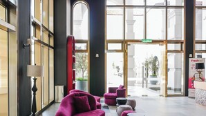 Un'ampia hall dall'arredamento moderno, con una poltrona rossa, diversi poggiapiedi e un'ampia entrata in vetro.