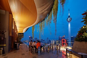 An outdoor seating area with tables and chairs, a view of the city skyline, and a prominent tower in the background. - 22 Macalisterz by Mykey (George Town)