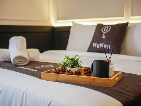 Una cama hecha con cuidado, una bandeja con piñas, una pequeña planta en maceta y una taza negra.