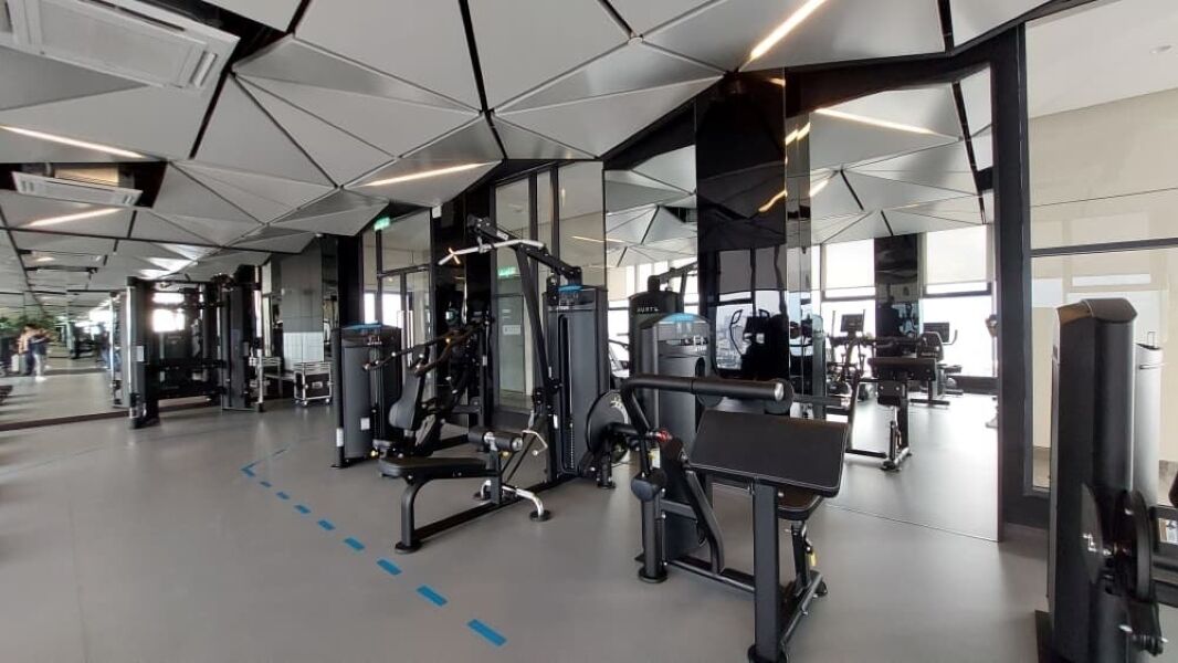 A modern gym with various exercise machines, large windows, and a clean, spacious layout.