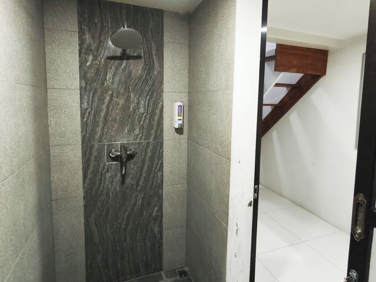 A shower with a marble wall, a control panel, and a wooden staircase in the background.