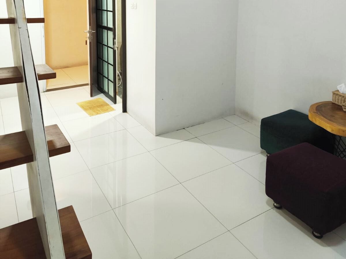 Una habitación limpia y moderna con piso de baldosas blancas, un banco de madera, una mesita redonda con una cesta y dos otomanas coloridas.