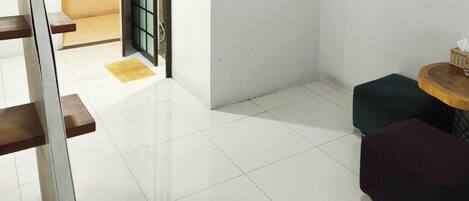 Una habitación limpia y moderna con piso de baldosas blancas, un banco de madera, una mesita redonda con una cesta y dos otomanas coloridas.