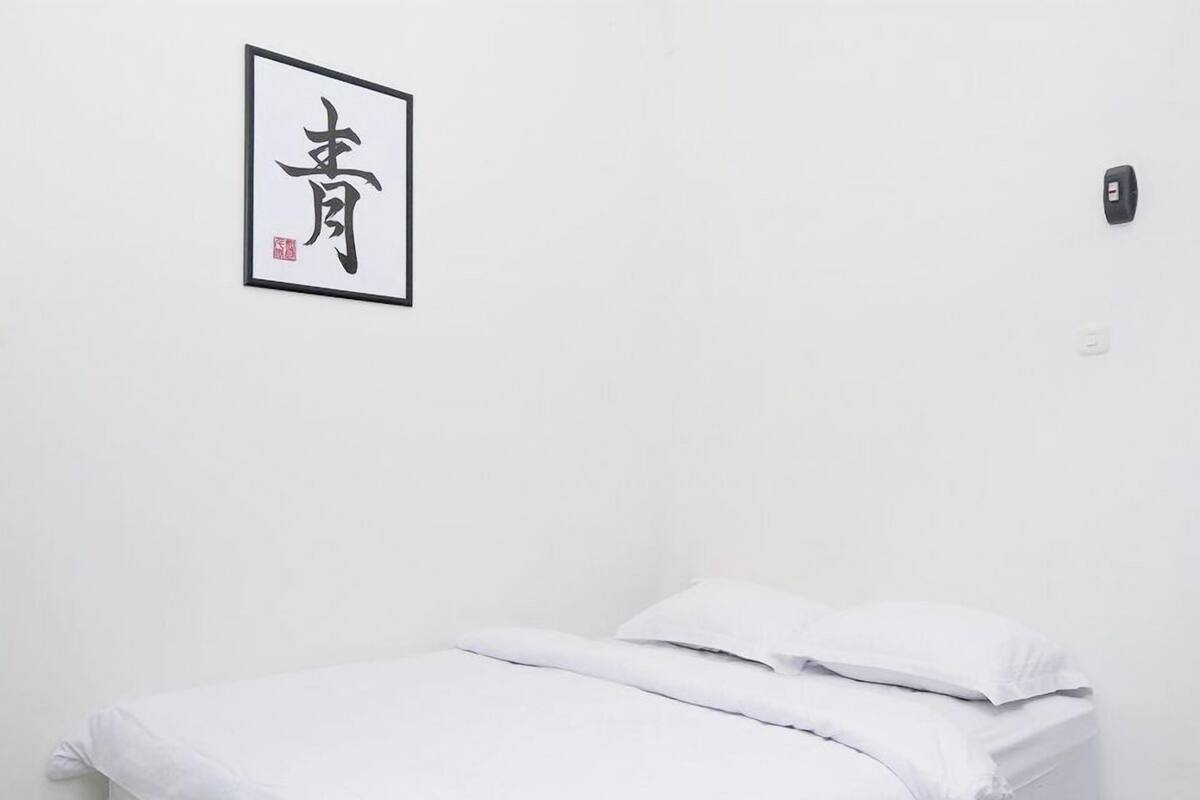 A neatly made bed with white bedding in a room with a plain white wall.
