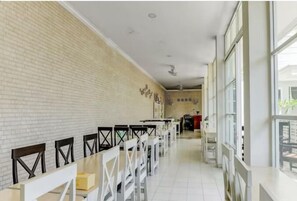 A long corridor with white tiled floors, white walls, and a brick accent wall. There are rows of white tables and black chairs along the corridor. - Padekostay (Tulungagung)