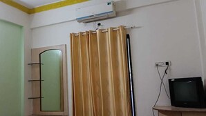 A room with a green door, a mirror, a television on a wooden stand, and a curtain rod with curtains. - Vaishali Lodge (Pune)