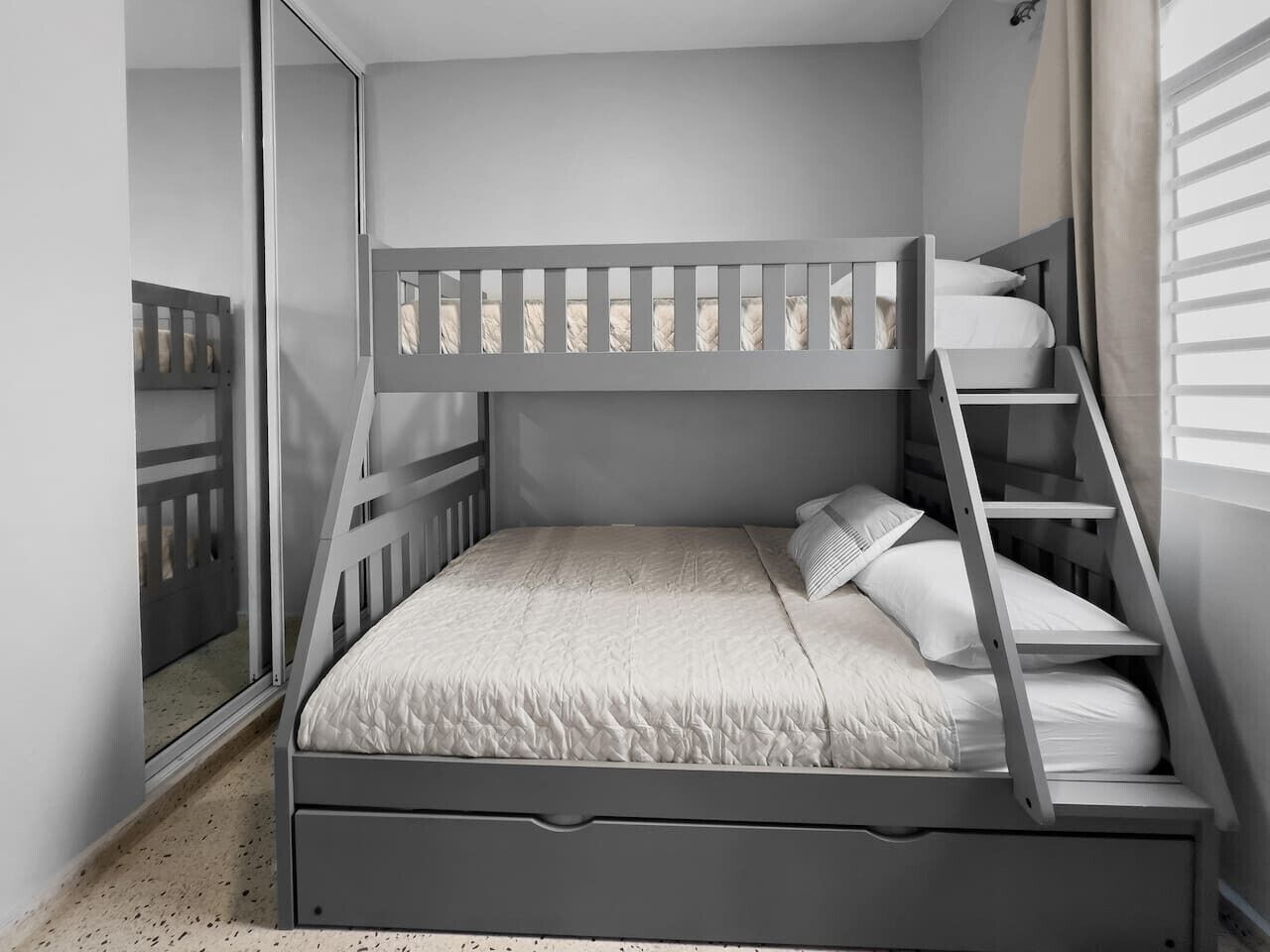 A bunk bed with a ladder, a window with blinds, and a mirror on the wall.