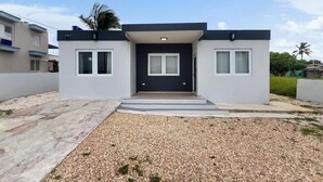 Une maison moderne à deux étages, avec une porte d’entrée sombre, des murs blancs et une allée gravillonnée.