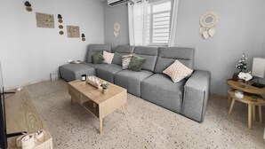 Un salon moderne avec un canapé gris, une table basse en bois et une petite table d’appoint avec une lampe.