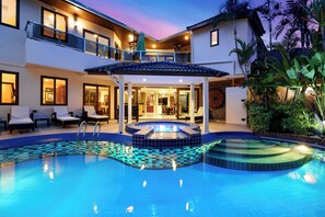 Una casa de dos pisos con piscina, mobiliario exterior y un porche cubierto.