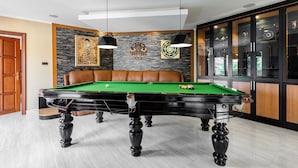 Una mesa de billar en una habitación con un sofá de cuero marrón, una pared de piedra con obras de arte y un aparador con puertas de cristal.