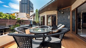 Un balcón con muebles de mimbre, una mesa de vidrio y vistas a edificios altos.