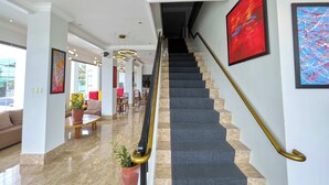 Un moderno vestíbulo de hotel con suelo de mármol, una escalera con barandilla dorada y obras de arte contemporáneas en las paredes.