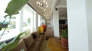 Un moderno vestíbulo de hotel con un sofá, sillas, una mesa de madera y una planta grande.