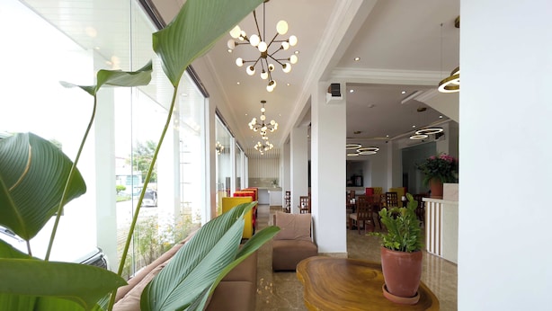 Un vestíbulo de hotel moderno con ventanas amplias, un sofá, una mesa de madera y una planta en maceta.