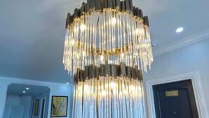 Un candelabro con varios niveles y elementos colgantes, una puerta con el número 310 y una obra de arte enmarcada en la pared.