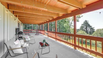 Un espacio de estar al aire libre techado con sillas y mesas, techo de madera y vista a árboles.