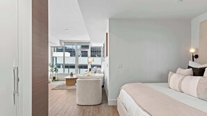 A modern hotel room with a large bed, a round table, and a view of the cityscape.
