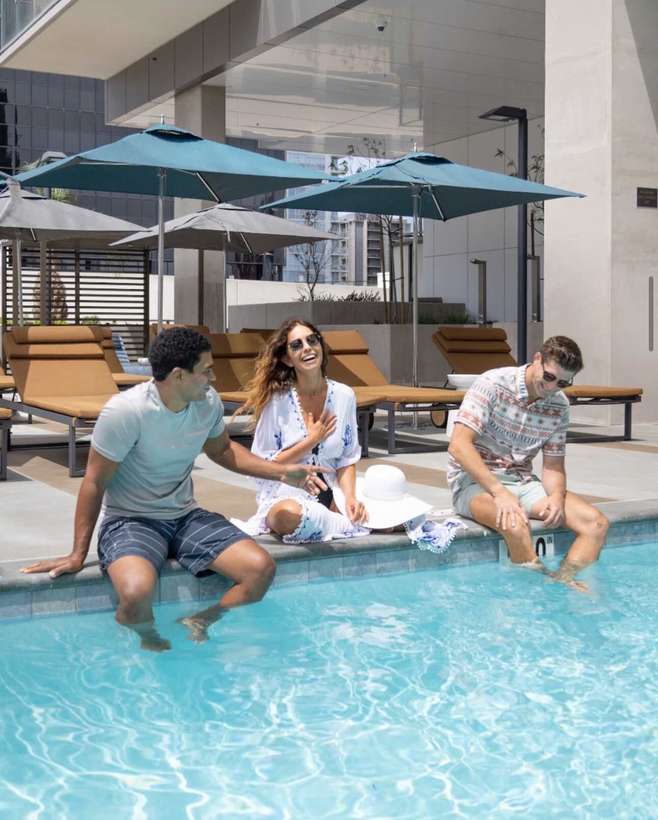 A pool area with lounge chairs and umbrellas, a clear pool, and a modern building in the background.