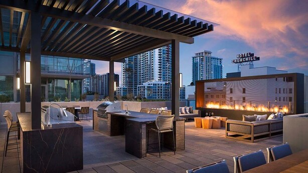 A rooftop bar with a grill, seating, and a fire feature.