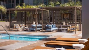 A poolside area with lounge chairs, a pool, and a covered seating area with plants.