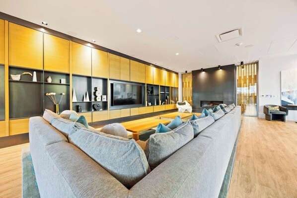 A modern living room with a long grey sofa, wooden coffee table, and built-in shelving with decorative items.