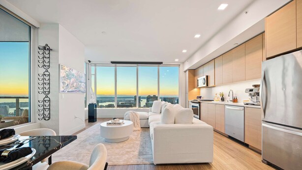A modern living room with a sofa, a coffee table, and a dining area with a table set for two. - Luxury 39th-Floor Sky Residence · Ocean Views (San Diego)