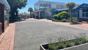 A courtyard with a paved area, a building with large windows, and some greenery. - Beverley bay 2-Bed Caravan, Sleeps 6, Pet Friendly (Paignton)