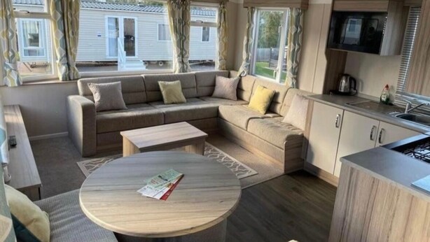 A compact living space with a sofa, a round coffee table, and a kitchenette. - Beverley bay 2-Bed Caravan, Sleeps 6, Pet Friendly (Paignton)