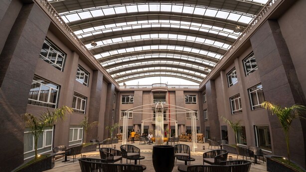 A spacious indoor courtyard with a high glass ceiling, modern seating arrangements, and a central water feature. - Chokar Dhani Resort (Kalmeshwar)