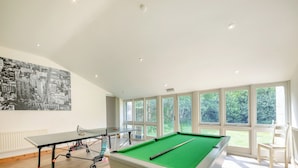Une table de billard recouverte d’un drap vert, une table de ping-pong et une fresque représentant un paysage urbain sur le mur.
