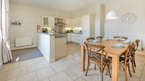 Une cuisine moderne avec des meubles blancs, un îlot central et un coin repas comprenant des chaises et une table en bois.