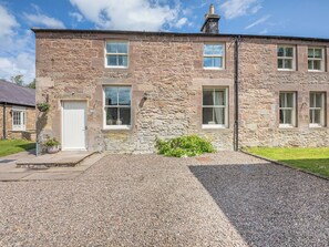 A stone building with a white door, multiple windows, and a gravel driveway. - Swinney Cottage - UK49893 (Doxford, near Embleton)