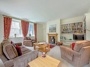 A living room with a fireplace, sofa, armchair, bookshelf, and a television. - Swinney Cottage - UK49893 (Doxford, near Embleton)