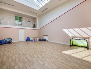 Um espaço interno amplo com teto alto, varanda e área de recreação com brinquedos coloridos.