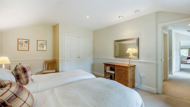 Une chambre avec deux lits, une commode, un miroir et une porte donnant sur une autre pièce.