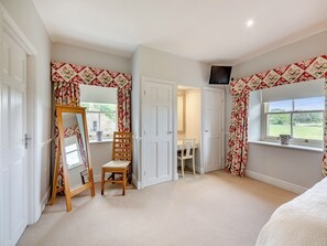 A bedroom with a large mirror, a wooden chair, a small table, and a window with a view of greenery. - Doxford House - UK49888 (Doxford, near Embleton)