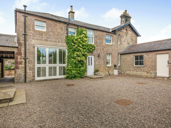 A stone house with a large window, a door, and a gravel driveway.