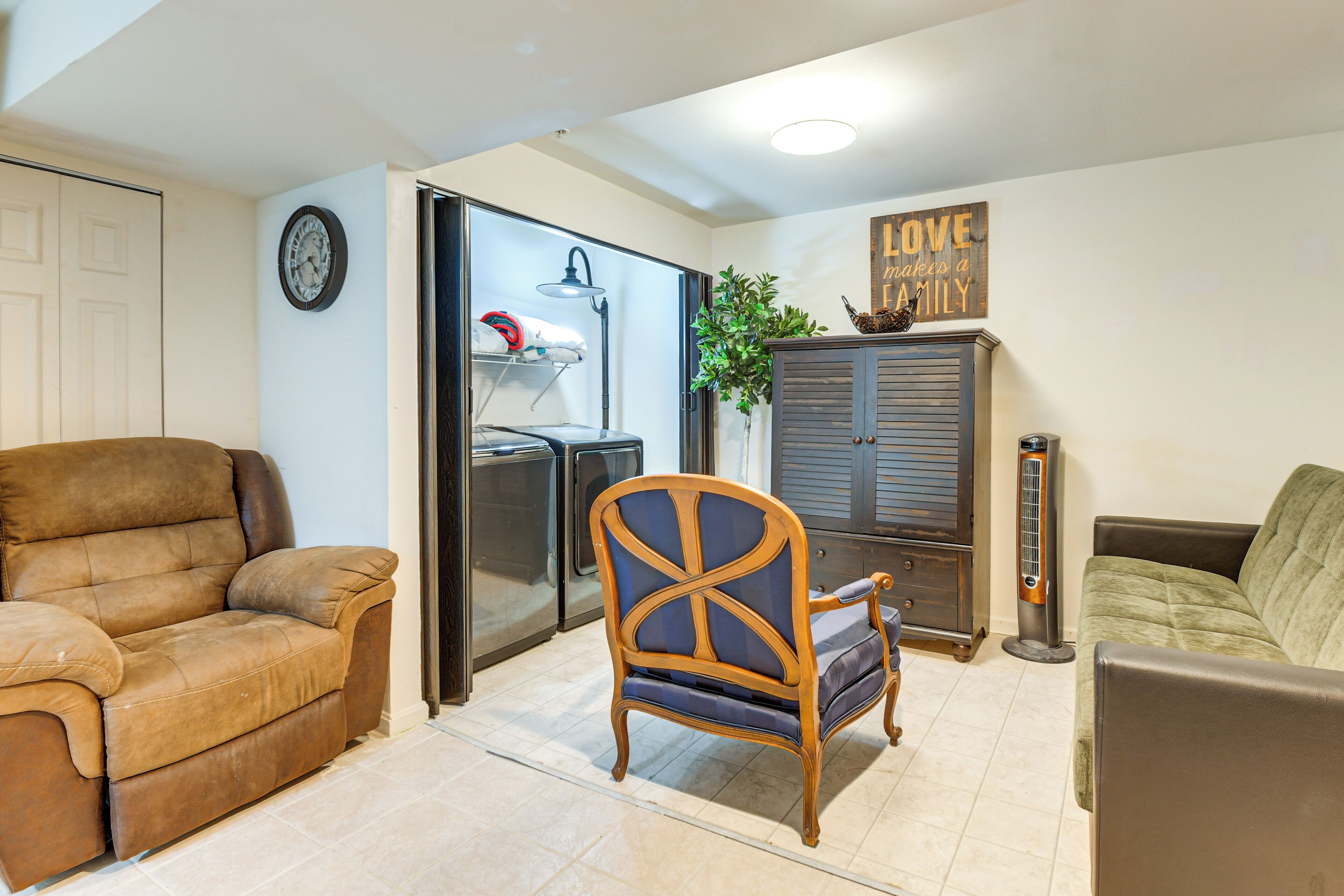 A living room with a brown sofa, a wooden chair, a green sofa, a cabinet, a heater, and a clock on the wall.
