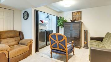 A living room with a brown sofa, a wooden chair, a green sofa, a cabinet, a heater, and a clock on the wall.