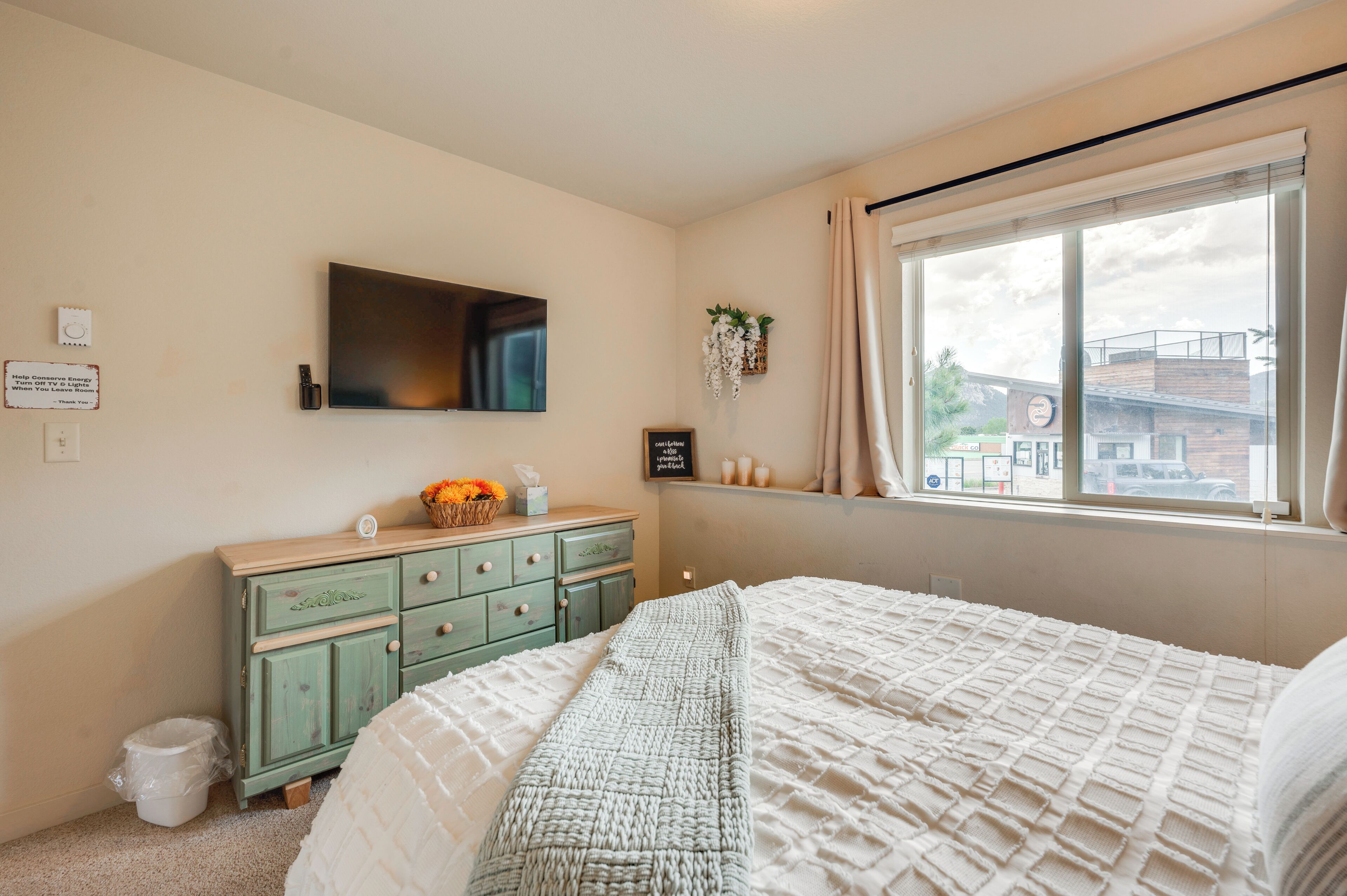 Una camera da letto con un letto, una cassettiera, una finestra con tende e una TV a parete.