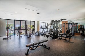 Un gimnasio amplio con diversos equipos de ejercicio, ventanas grandes y un banco.